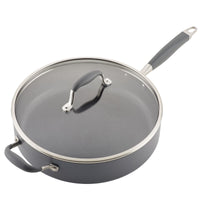 A nonstick skillet with a glass lid and dark gray rubber handles. The pan is round, with a long handle on one side and a short grip handle on the other. The lid has a stainless-steel rim and a matching handle.