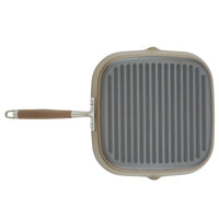 A square grill pan with a ribbed surface and a long, brown handle. The pan is gray, and the handle has a metallic connection to the pan. The design is modern and minimalistic.