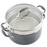 A large, gray cooking pot with a steamer insert and a transparent glass lid. The pot has black handles on the sides and lid, and the insert has multiple holes for steam to pass through.