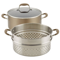 A three-piece cookware set featuring a large pot with a glass lid and soft handles, accompanied by a metal steamer insert with perforated sides and matching handles. The items are designed for versatile cooking.