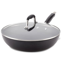 A large black nonstick frying pan with a shiny glass lid and a sleek black handle. The lid has a metal rim and a small black handle in the center. The pans design combines functionality with a modern aesthetic.