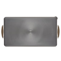 Rectangular metal baking sheet with handles on each side, featuring a non-stick surface and a subtle circular pattern in the center. The handles have a light brown, heat-resistant grip.