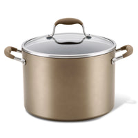 A large, metallic bronze pot with a matching lid and brown handles. The lid has a clear glass center and a silver rim, featuring a brown handle on top. The design is sleek and modern.
