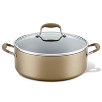 A large, round, gold-colored cooking pot with two side handles and a clear glass lid featuring a handle on top. The pot is placed on a white background.