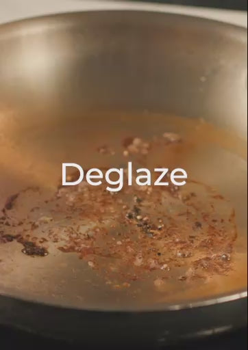 A 17-second instructional video titled "Deglaze" featuring a chef in a pink shirt. After searing meat in an Anolon EverLast Clad Stainless Steel frying pan, the chef pours liquid into the hot pan to loosen the browned bits (fond). The video shows the chef using a whisk to easily stir and incorporate the flavorful drippings into a smooth sauce, highlighting the pan's responsive heat control and non-reactive surface.