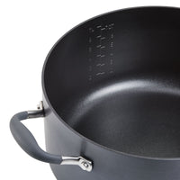 A large, dark-colored cooking pot with a non-stick interior is shown at an angle. It has measurement markings inside and features a handle with a rubber grip.