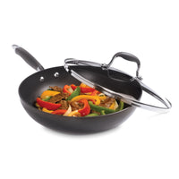 A black non-stick frying pan with a glass lid contains colorful bell peppers and slices of beef. The pan is shown against a white background.