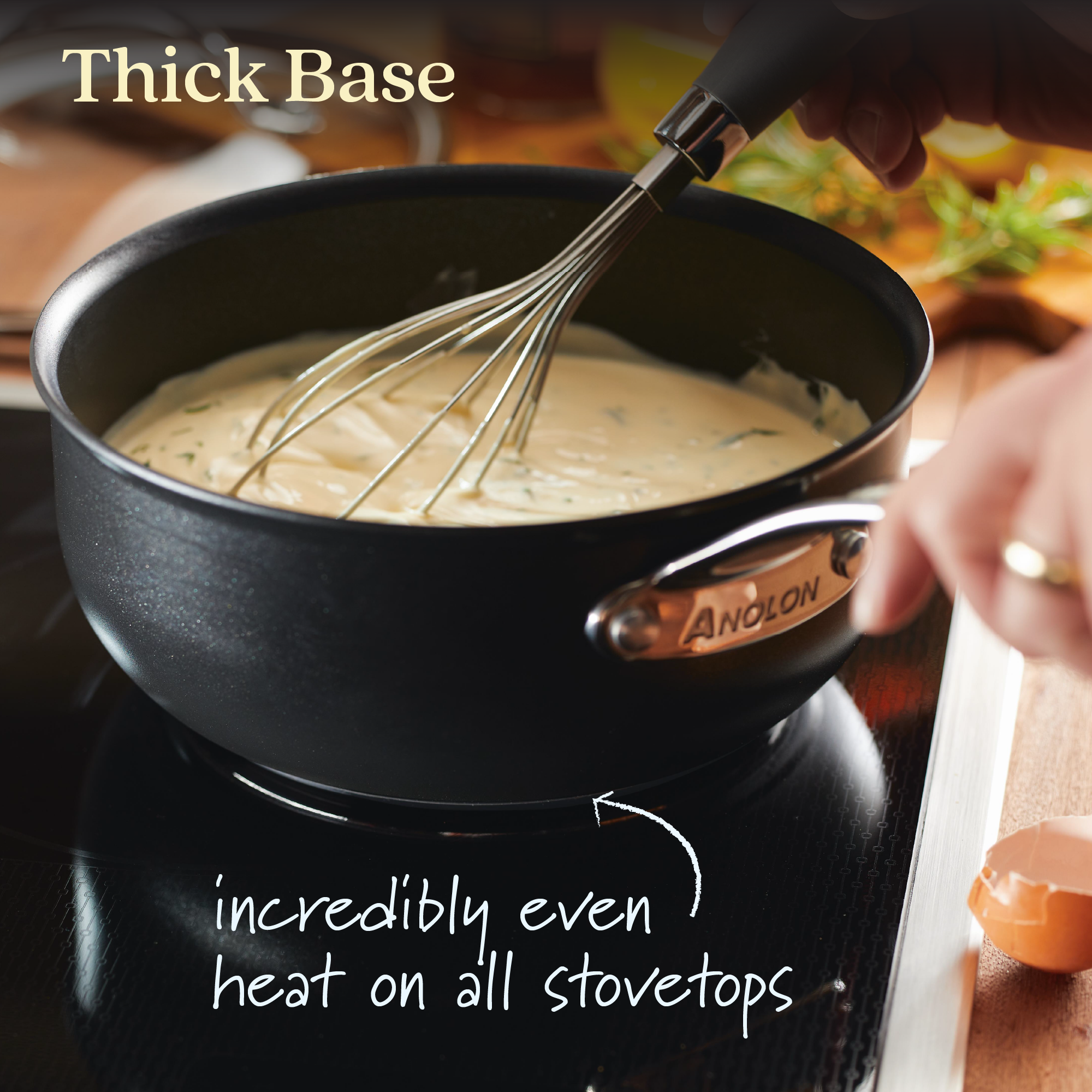 A 2.5-quart Hybrid Nonstick Saucier Pan by Anolon X with a metal whisk stirs creamy sauce on a stovetop. Text reads: Thick Base and incredibly even heat on all stovetops. A hand holds the pot, highlighting its SearTech™ technology and metal utensil safe design.