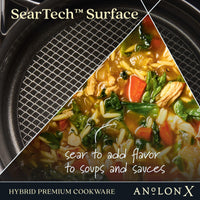 Close-up of Anolon Xs 3-Quart Hybrid Nonstick Saucepan With Lid, showing half with a textured nonstick surface and the other half with vegetable soup. Text reads, SearTech technology: sear to enhance flavor in soups and sauces—metal utensil safe.