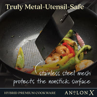 A metal spatula stirs shrimp, sliced peppers, and vegetables in an Anolon X 10-Inch Hybrid Nonstick Wok With Lid, featuring a stainless steel base and mesh surface. The text states Truly Metal-Utensil-Safe, emphasizing its durability.