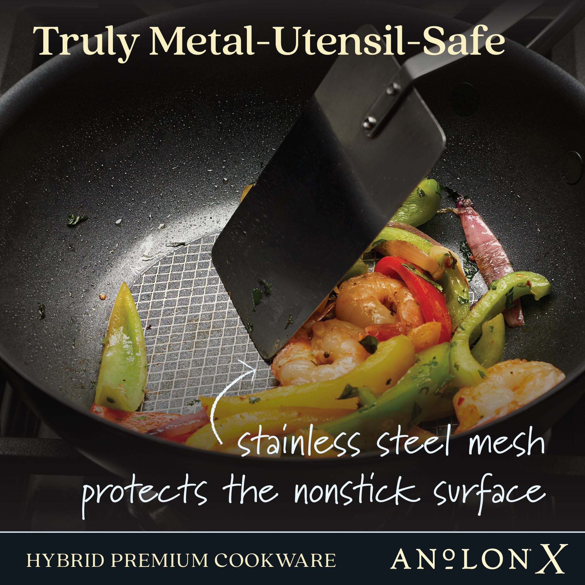 A metal spatula stirs shrimp, sliced peppers, and vegetables in an Anolon X 10-Inch Hybrid Nonstick Wok With Lid, featuring a stainless steel base and mesh surface. The text states Truly Metal-Utensil-Safe, emphasizing its durability.