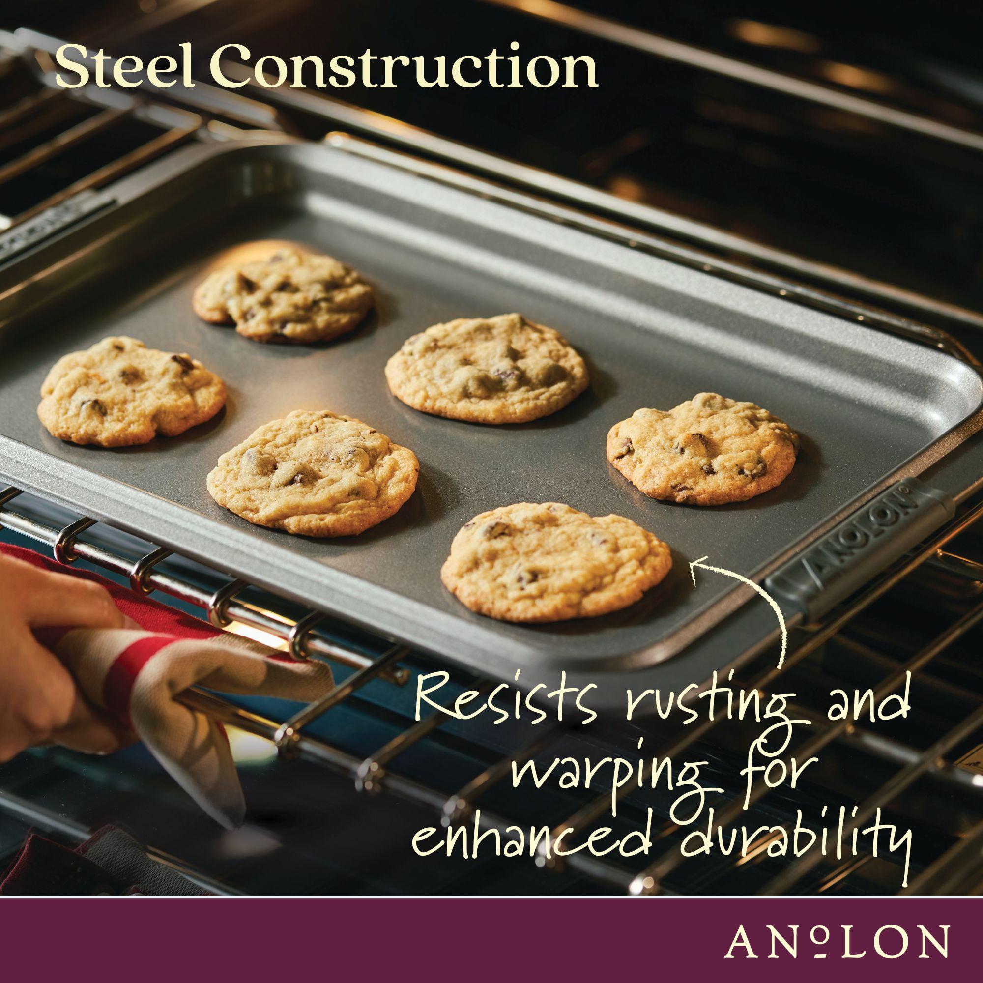 A person places an Advanced 11 x 17-Inch Baking Sheet and Cooling Rack Set with six cookies in the oven. Text reads: “Steel construction resists rusting and warping for durability.” The Advanced brand name is shown at the bottom.