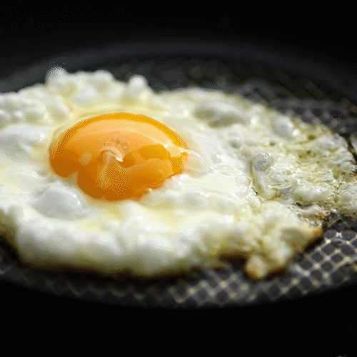 A sunny-side-up egg frying in a pan.