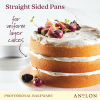 A three-layer cake with white frosting is adorned with figs and cherries. The text reads "9-Inch Aluminized Steel Round Cake Pan" by Pro-Bake in the bottom corner. Designed with premium aluminized steel, this pan guarantees even heat distribution for flawless results.