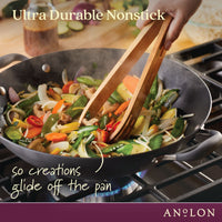 A person uses wooden tongs to stir-fry a colorful mix of vegetables in an Advanced Home 14-Inch Wok with Side Handles on the stove. The image highlights the ultra durability and nonstick quality of this hard-anodized flat bottom wok, showcasing the brand's commitment to excellence.