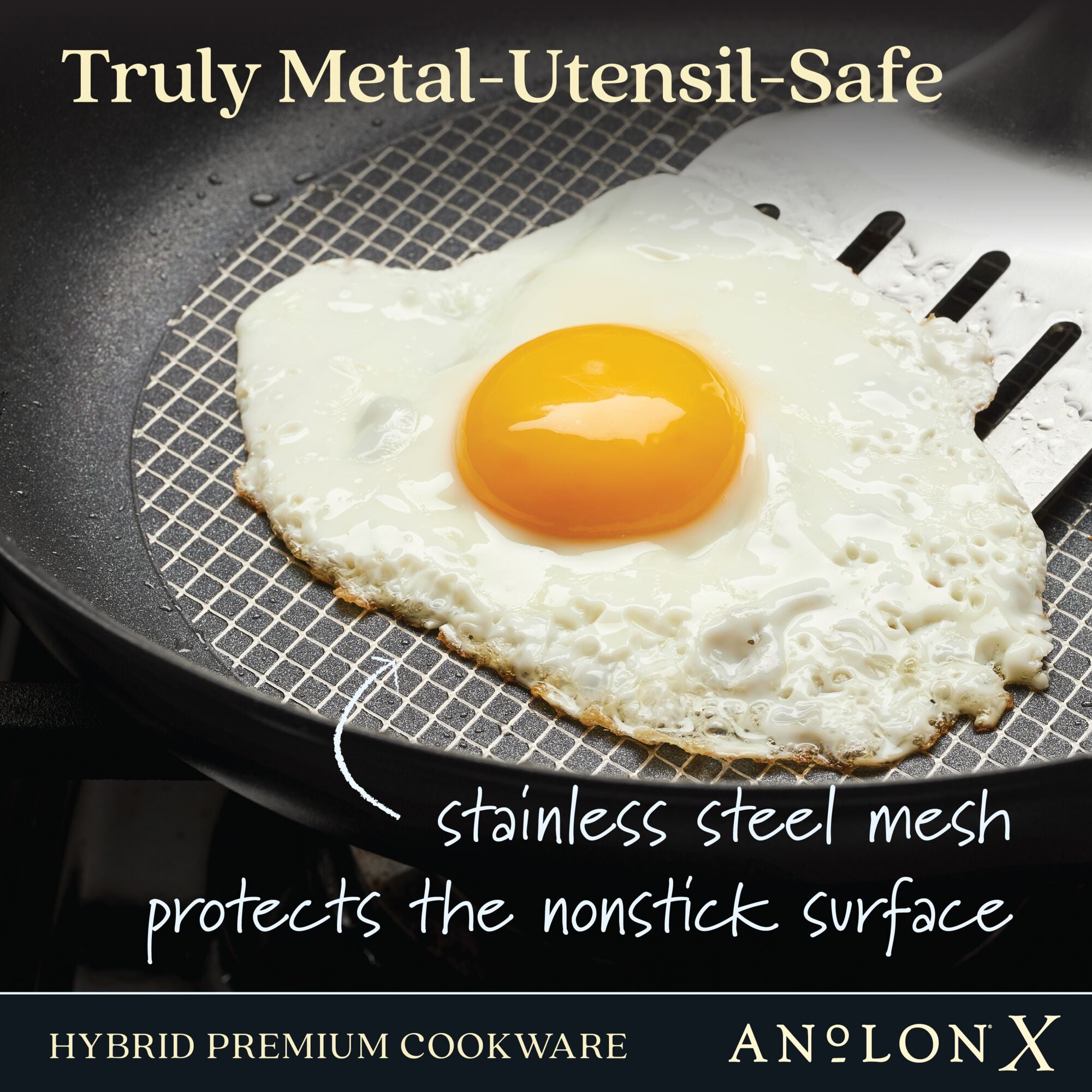 An egg is lifted with a metal spatula on a pan featuring a SearTech™ surface and stainless steel mesh. Text reads: Truly Metal-Utensil-Safe, stainless steel mesh guards the PFOA-free nonstick surface, from Anolon Xs 10-Piece Hybrid Nonstick Cookware Set.