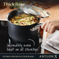 A hand lifts the lid off a black Anolon X 3-Quart Hybrid Nonstick Saucepan on a stove, revealing a dish with pecans and herbs. Text reads, Thick base, incredibly even heat on all stovetops with SearTech technology. A white towel is beside the pot. Known for its premium nonstick finish.