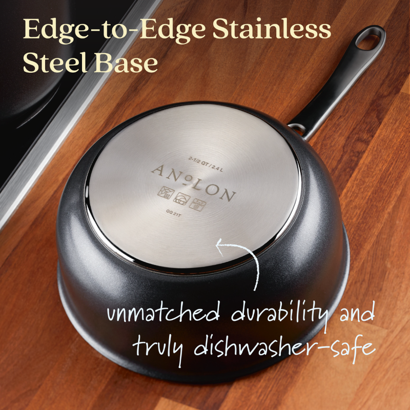 A 2.5-Quart Hybrid Nonstick Saucier Pan by Anolon X is displayed upside down on a wooden surface, showcasing its SearTech™ stainless steel base with Edge-to-Edge Stainless Steel Base and emphasizing unmatched durability and truly dishwasher-safe.