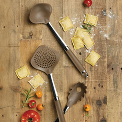 A rustic wooden surface features the Tools and Gadgets 3-Piece Pasta Tool Set, with its brown kitchen utensils boasting comfortable handles. Uncooked ravioli is artfully scattered across the scene, surrounded by cherry tomatoes and sprigs of rosemary to create a charming culinary display.