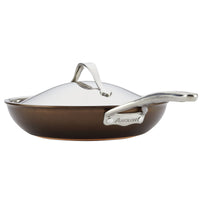 Side view of a bronze-colored frying pan from the Nouvelle Luxe 11-Piece Cookware Set, crafted with ultra-tough hard-anodized aluminum. It features a shiny stainless steel lid and handle, elegantly engraved with the name Anolon. Emphasizing exceptional copper performance, the pan is displayed against a white background.