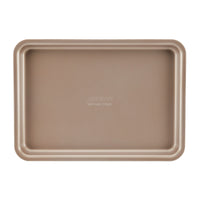 A beige, rectangular nonstick baking tray from the Gourmet 3-Piece Cookie Pan Set is viewed from above against a white background. The center of the tray features a subtle embossed logo and specifications, making it perfect for baking homemade cookies.