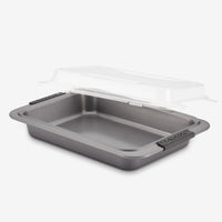 The Advanced 9 x 13-Inch Cake Pan with Lid features black handles and a clear plastic lid, shown slightly raised above the pan against a plain white background.