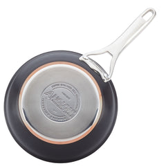 The image showcases a black frying pan from the Nouvelle Luxe 11-Piece Cookware Set, flipped to show its silver base made of hard-anodized aluminum. The base is inscribed with brand and product information, and features a sleek metallic handle that extends elegantly. A copper ring near the edge boosts its functionality and visual allure.