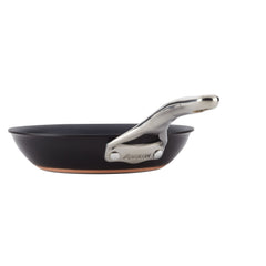 A side view of a black frying pan from the Nouvelle Luxe brand reveals its shiny silver handle. Crafted from ultra-tough hard-anodized aluminum, it features a gleaming copper-colored bottom edge for a sleek, modern look. With the Infinity Slide™ Nonstick System, it promises superior performance as part of the 11-Piece Cookware Set.