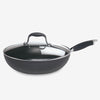 The Advanced 12-Inch Covered Ultimate Pan is a black nonstick stir fry pan with a long handle and clear glass lid, perfect for one-pan meals, shown on a white background.
