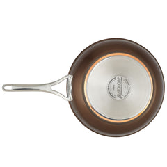 Top view of a nonstick frying pan from the Nouvelle Luxe 11-Piece Cookware Set, showcasing copper performance and a silver base stamped with brand details. The pan has a brown exterior and a long, shiny metallic handle with a hanging hole.