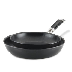 A pair of dark non-stick frying pans from the SmartStack Frying Pan Set, designed for induction cooking and featuring sleek black handles, are stacked together. The larger pan supports the smaller one on top, showcasing their smooth, curved design against a plain white background.