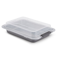 The Advanced 9 x 13-Inch Cake Pan with Lid features a versatile nonstick rectangular design, a clear plastic lid, and black side handles, shown on a white background.