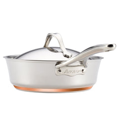 A stainless steel saucepan with a copper base from the Nouvelle Luxe 11-Piece Mixed Metals Cookware Set offers excellent nonstick performance. It is designed with a long handle and comes with a matching lid, and the Nouvelle Luxe brand name is elegantly engraved on the side, exemplifying high-quality copper cookware.