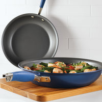 The Advanced Home 10.25 & 12.75-Inch Frying Pan Set is shown: one pan with cooked shrimp and vegetables on a wooden board, the other pan empty and resting against a white tiled wall in the background.
