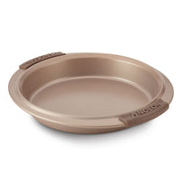The 9-Inch Round Cake Pan from Advanced features a light brown finish and signature design. It includes a nonstick surface and silicone grips on both sides for easy handling, along with slightly raised edges to ensure perfect baking every time.
